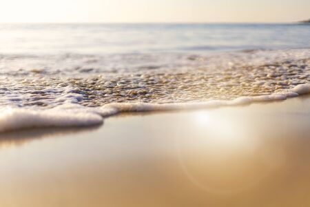Sunset beach wave from sea come to beach with sun light reflect on water sea soft focus and focus selective to soft wave and sand. with copy space for text or design.の写真素材