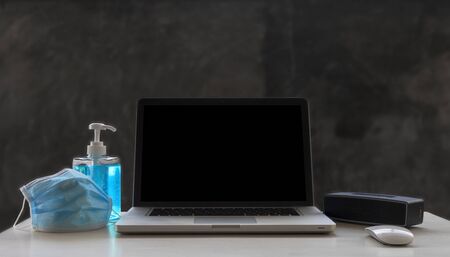 Laptop, mouse, speaker, alcohols gel and Medical mask on white wood table and  raw cement  background with copyspace for text or design.の写真素材