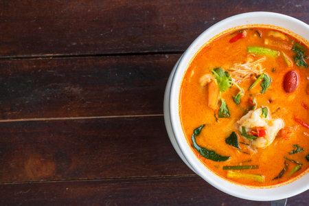 top view Tom Yam kung Spicy Thai soup with shrimp in white bowl on wood table. With copy space for...