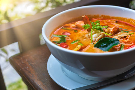 Tom Yam kung Spicy Thai soup with shrimp in white bowl on wood table. With copy space for text or...