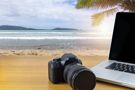Digital camera and laptop on wood table with sea and sky background. With copy space for text or design.の写真素材