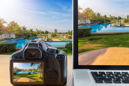 Picture of laptop computer and back screen digital camera on wood table with garden and pool...