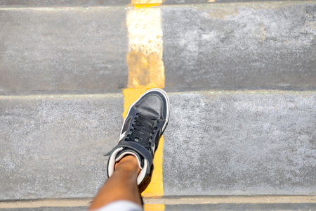 Man legs with long sneakers walking down public stair with yellow line in the city. 