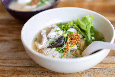 Soup with thin noodle, pock, pock stick, mushroom, vegetable in white bowl on wood table. with copy...