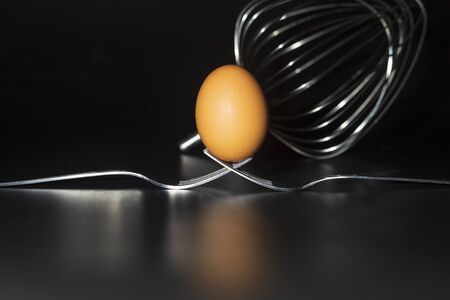Organic fresh egg standing on two joined fork on black backgroundの写真素材
