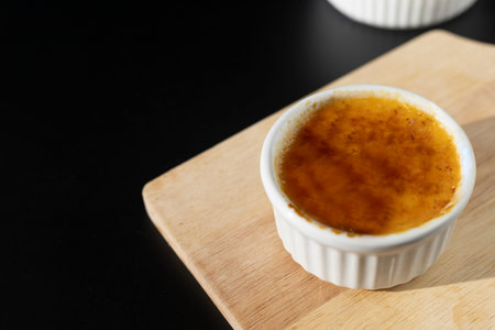 Close up homemade creme brulee in white ramekin  with sugar burn top up on black background with copy space. French dessert creme bruleeの写真素材