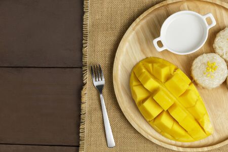 Top view Yellow half  mango with small fork. Mango fruit cubes on the wooden table. Tropical fruit asia. Fresh yellow mango peel and Sliced cubes on wood butcher. Dessert fruit.の写真素材