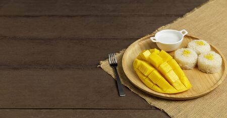 Yellow half  mango with small fork. Mango fruit cubes on the wooden table. Tropical fruit asia. Fresh yellow mango peel and Sliced cubes on wood butcher. Dessert fruit.の写真素材