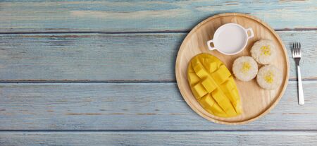Top view Yellow half  mango with small fork. Mango fruit cubes on the Blue wooden table. Tropical fruit asia. Fresh yellow mango peel and Sliced cubes on wood butcher. Dessert fruit. Tropical fruit summer concept.の写真素材