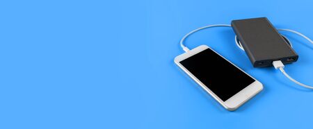Top view smartphone charging with power bank on blue background with copy space. Smartphone charging with power bank by white USB cable.の写真素材