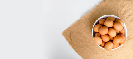 Top view Fresh chicken eggs in white bowl on white color wooden table with copy space. Uncooked raw...