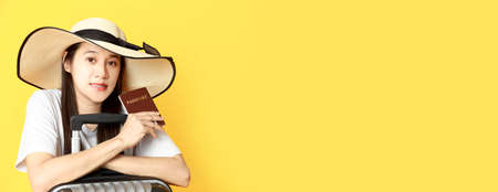 Asian women long hair wear Straw hat with black ribbon in hand holding passport book and travel bag with copy space banner. Young girl ready to travel with suitcase and passport on yellow background. Summer travel concept.の写真素材