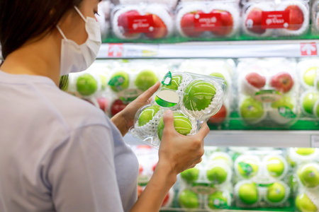 Women long hair wear protective face mask hands holding green apples ipackage. Asian female shopping...