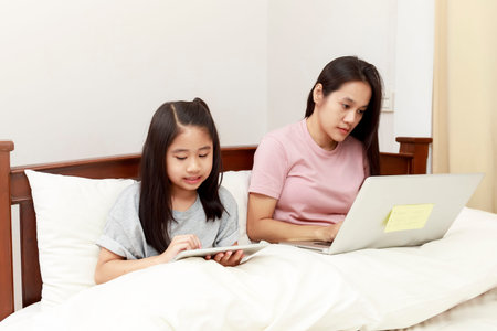 Asian mother and daugther looking laptop and tablet on bed in bedroom. Business women woking with...