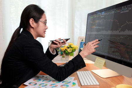 Business women holding smart phone to speak with partner by speaker phone and analysis stock chart...