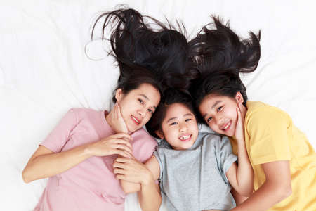 Asian family enjoy and relax on bed in bedroom. mother and daughters enjoy using laptop, tablet and smart phone together on bed.  Family concept.の写真素材