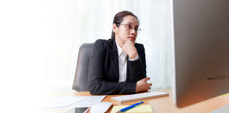 Business woman working in office with computer thinking analysis stock chart. business people working at home with PC screen. Business and finance ,work at home conceptの写真素材