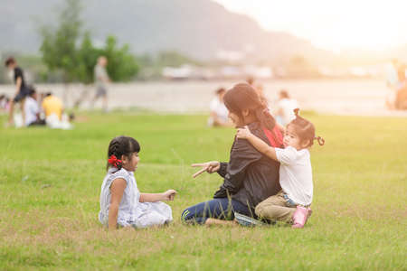 Family at park concept. Mother and her daughter sitting together and play hand at park. Happy family sitting  smiling and relax at park in the eveningの写真素材