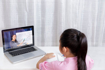 Asian little girl student learning via internet online class from school teacher duling covid-19...