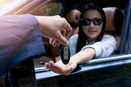 Close up of dealer giving key to new owner car. New car. Auto dealer giving woman automobile key for test drive on country road. Soft focus  smiling women try to test drive a car on road with dealer.の写真素材