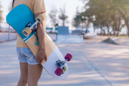 Close up on young women hand hold skateboard, surf skate on public skate ramp park background. Free relax skateboard surf skate trendy concept. Fashion portrait of female hands holding surf skateboardの写真素材