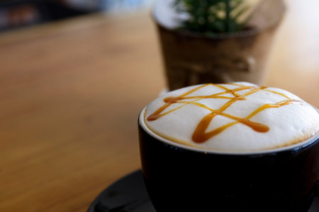 Close up hot cappuccino, latte, caramel macchiato on table with blur coffee shop background. Process...