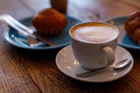 Close up hot cappuccino, latte on table with blur coffee shop background. Hot cappuccino coffee on wood table with blur croissant background. breakfast at coffee shop. softfocus select coffeeの写真素材