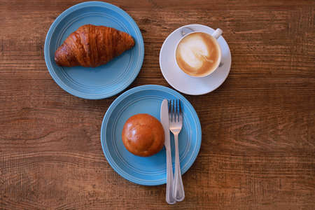 Top view hot cappuccino, latte on wood table with croissant and bun  in coffee shop. Breakfast at coffee shop.の写真素材