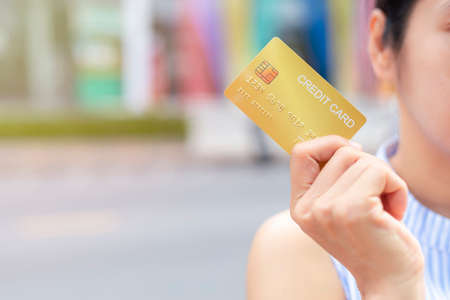 Woman hand holding gold credit card member card over blur department store background. Business, shopping, lifestyle concept. With copy spaceの写真素材