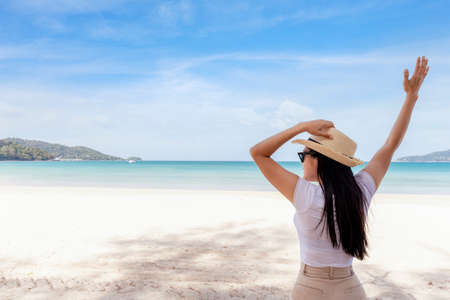 Portrait  middle shot view of woman stand in white T shirt and hat looking out towards blue ocean and sky, Women enjoy with beautiful sea view. Summer holiday vacation timeの写真素材