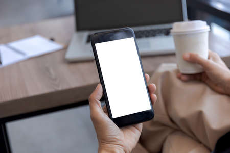Top view female hands holding smart phone with blank white screen. Women hands workspace, close-up hand holding smartphone blank screen for text and content at cafe coffee shopの写真素材