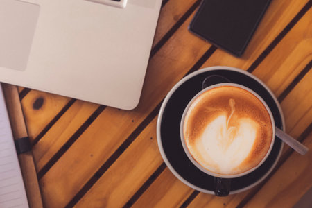 Top view hot coffee cup with blur laptop smarthphone and note book on wood table. office desk with...