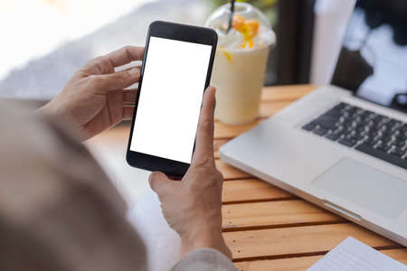 Top view female hands holding smart phone with blank white screen. Women hands workspace, close-up hand holding smartphone blank screen for text and content on wood table background.の写真素材