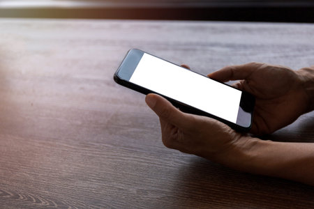 Top view female hands holding smart phone with blank white screen. Women hands workspace, close-up...