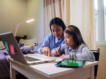Asian young little girl using pencil to do homework with her mother. Student kid writing  homework book. Girl use computer to study at home. Education homeschool  concept.の写真素材