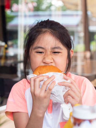 Asian little girl eating a burger. asian Children eat chicken cheese Hamburger.の写真素材