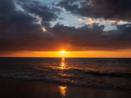 Beautiful sunset over the calm sea with cloud sky background. Sunset over tropical beach. Nature summer  concept. Peak sunset over sea with yellow light reflect on sea water. Tranquil seascape.の写真素材