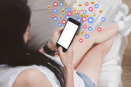 Asian woman sitting on sofa relaxing with cell phone white screen. young woman relax with social media only. women using the smart phone holding and typing with others through emoji and text online.の写真素材