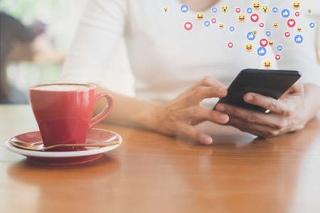Asian woman sitting in coffeeshop relaxing with cell phone. young woman relax with social media only. women using the smart phone holding and typing with others through emoji and text online.の写真素材