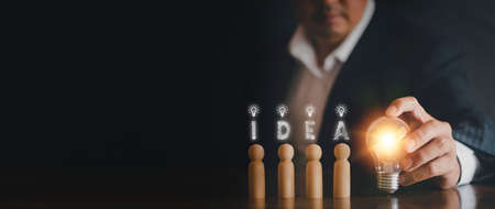Hand man holding light bulb with text i d e a and wooden doll. Innovation idea and knowledge concept. Hand of businessman holding light bulb with wooden dollの写真素材