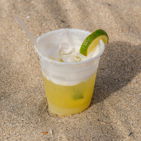 Plastic cup of margarita cocktail at the beach sand