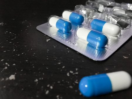 Blue and white capsule in foil panel on black wood table background