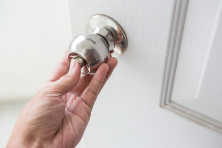 Hand holding a door knob on a white door
