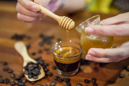 Woman hand pouring honey in a cup of coffeeの写真素材