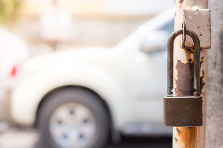 The padlock on the old iron fence gate and the background of the car parked outsideの写真素材