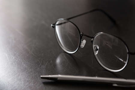 Selective focus of Pen, glasses, on black background and copy space with light and shadowの写真素材