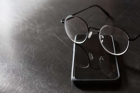 Selective focus of glasses,  smartphone on black background and copy space with light and shadowの写真素材