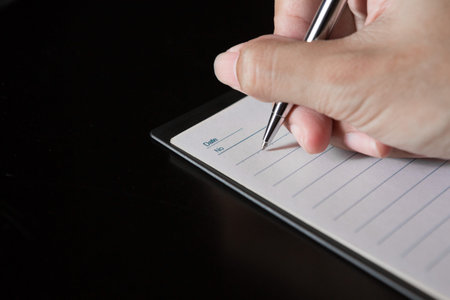 A hand holding a pen is writing on a notebook on black background and copy space