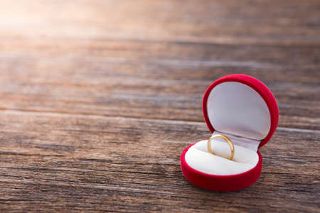 Gold ring in red ring box on wooden background with sunlightの写真素材