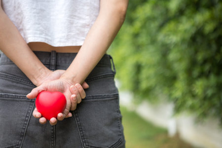 Selective focus of A woman with a heart shaped ball in her hand, hiding behind on blurred background...